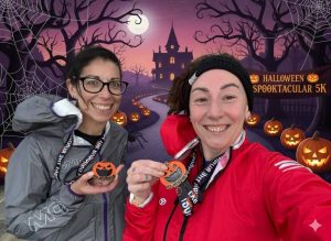 Two runners smiling and holding Halloween-themed virtual race medals in front of a spooky Halloween backdrop.
